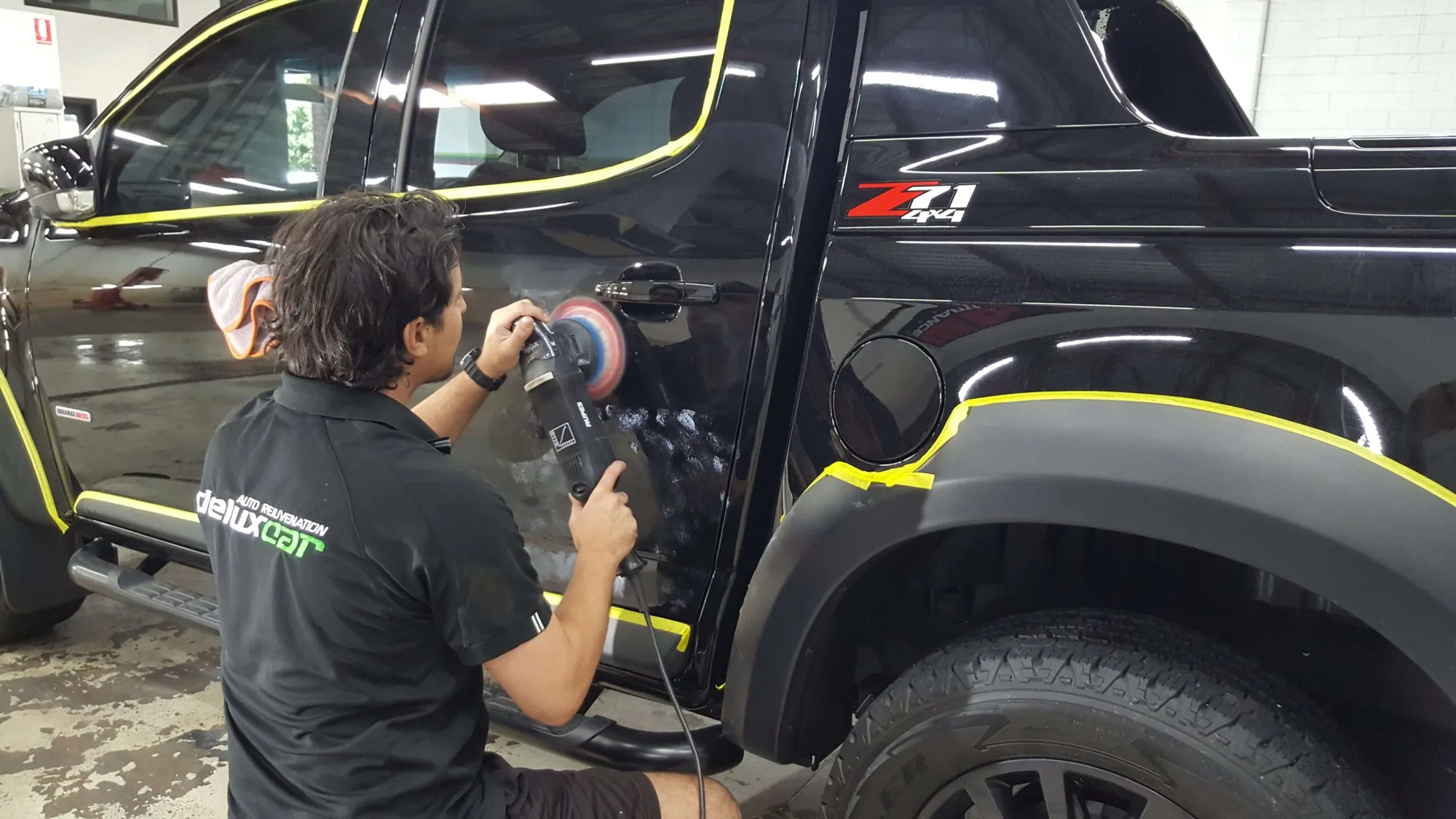 Ceramicar detailer cutting a masked panel of a black Ford Ranger with a rotary polisher