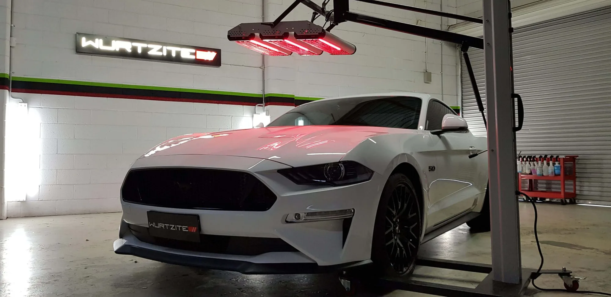 White Ford Mustang raised on the hoist under the Wurtzite sign in the Ceramicar paint protection bay